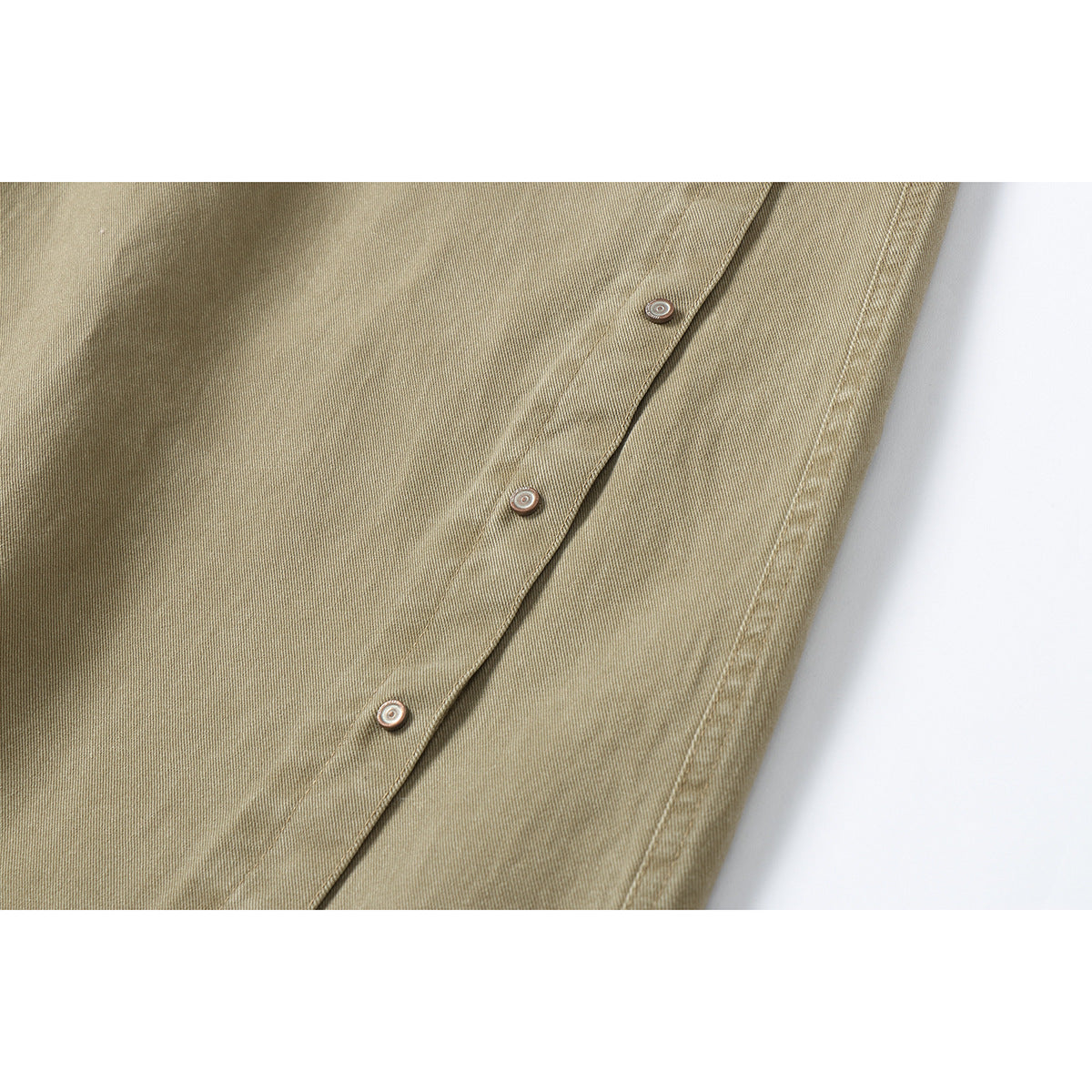 Close-up of tan pants fabric and a diagonal placket with three round metal buttons.
