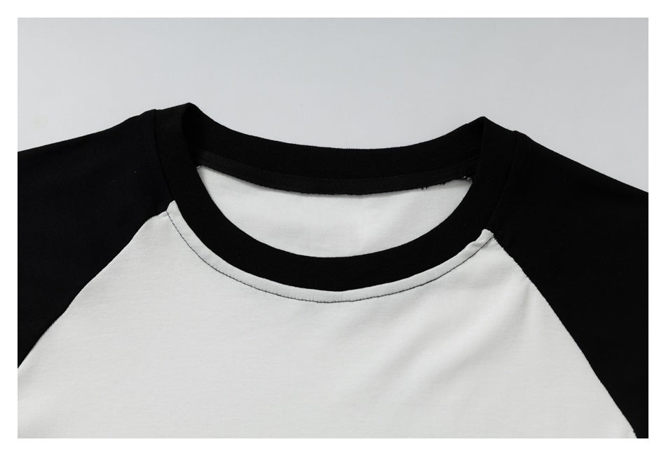 Close-up of a white raglan shirt with black shoulder panels and a black ribbed crew neck.