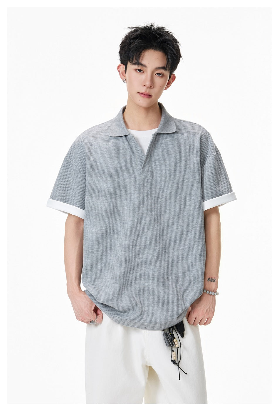 Front view of a model wearing a gray textured polo with a collar, open V-neck, and white turned-up cuffs.