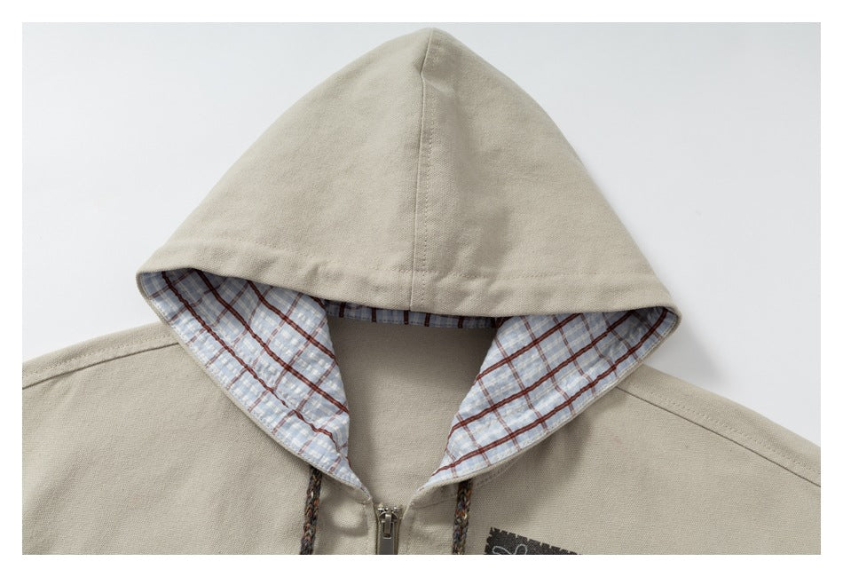 Close-up of a beige jacket hood with blue, white, and brown plaid lining, drawstrings, and a front zipper.