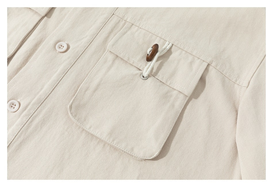 Close-up of a cream button-up shirt pocket with a white cord loop and brown toggle.
