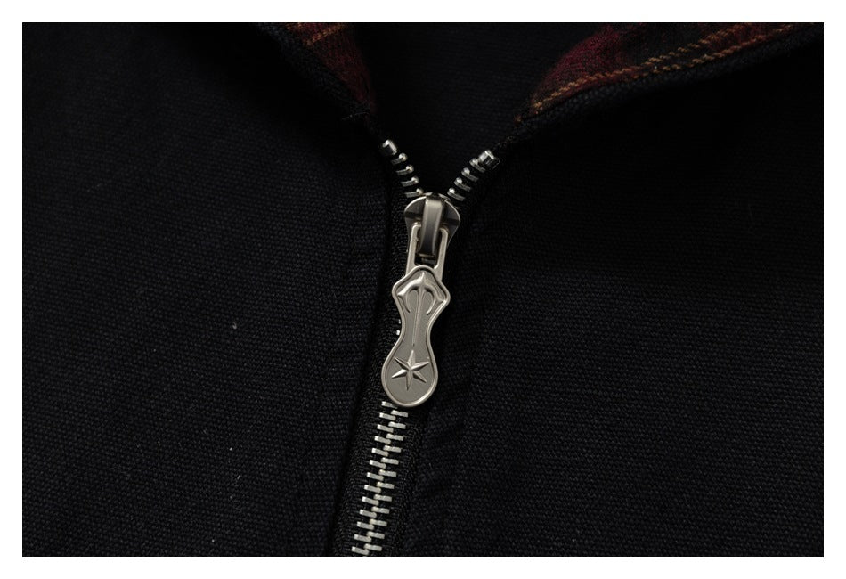 Close-up of the jacket's silver metal zipper and decorative pull against black fabric.