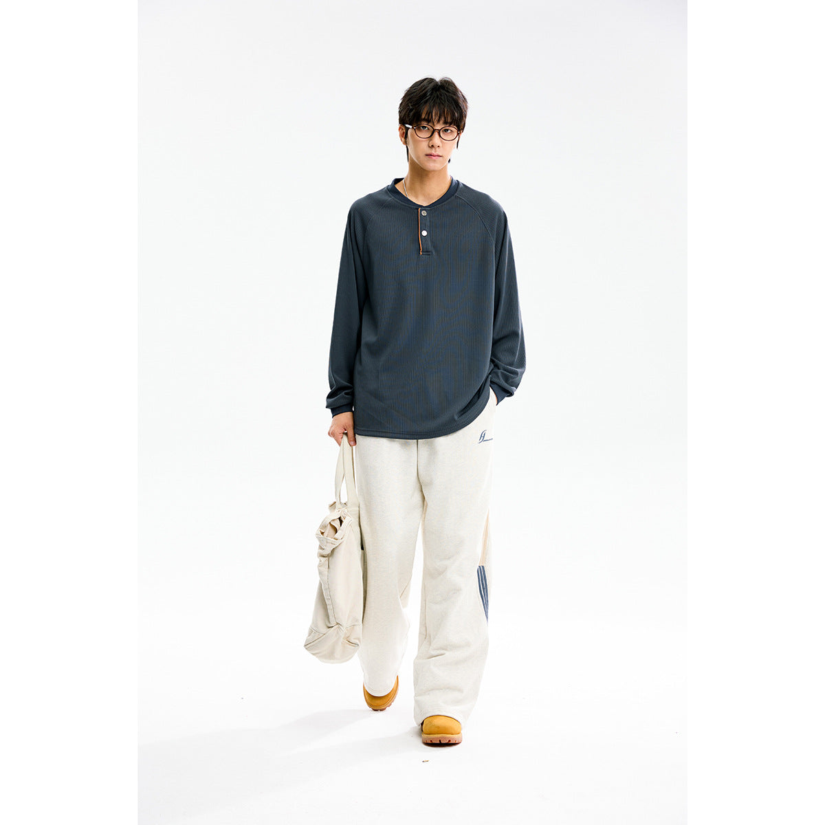 Model wearing a slate-blue long-sleeve Henley shirt with a two-button placket and loose cream pants.