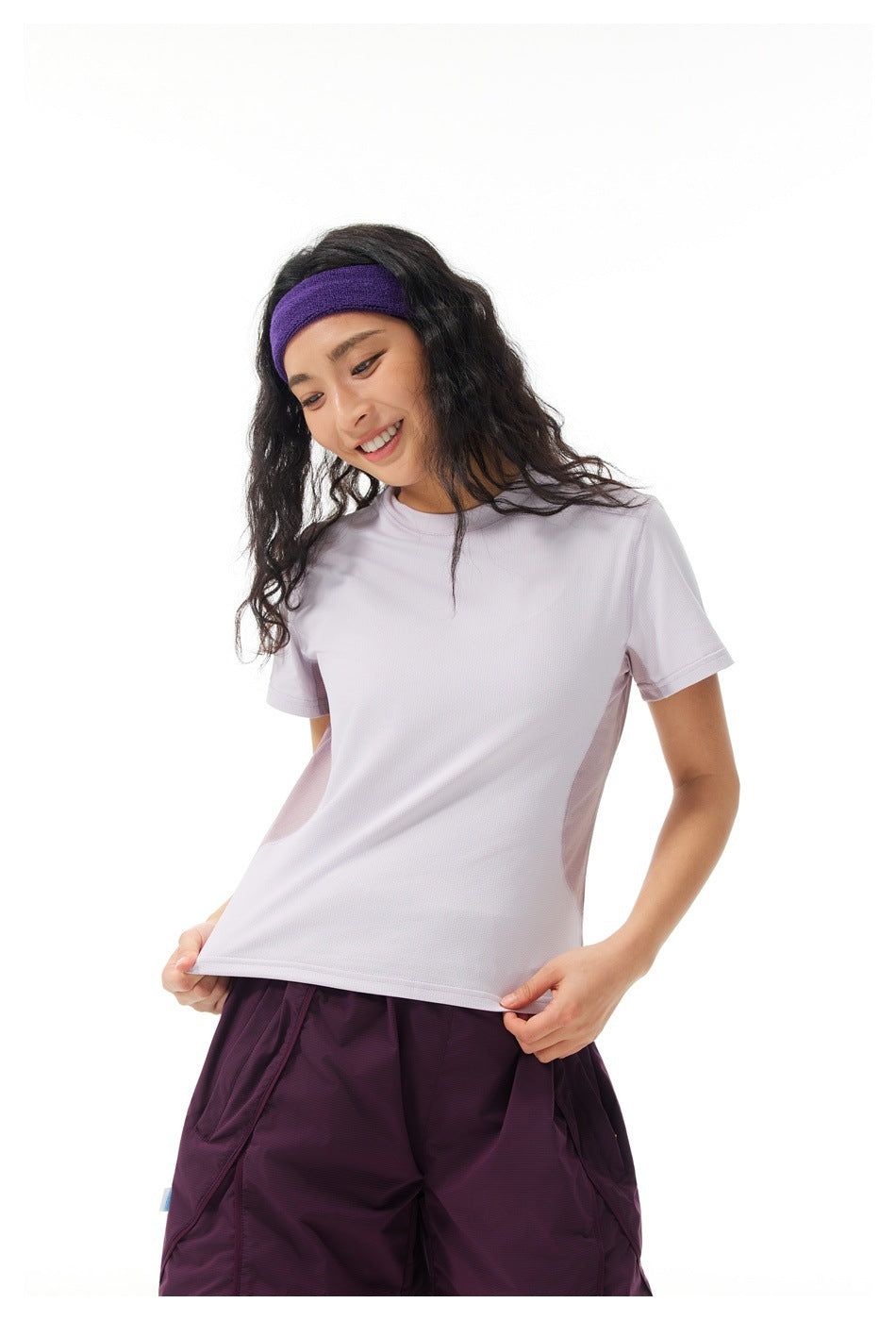 Closer front view of a woman wearing a light lavender short-sleeve shirt with plum shorts.