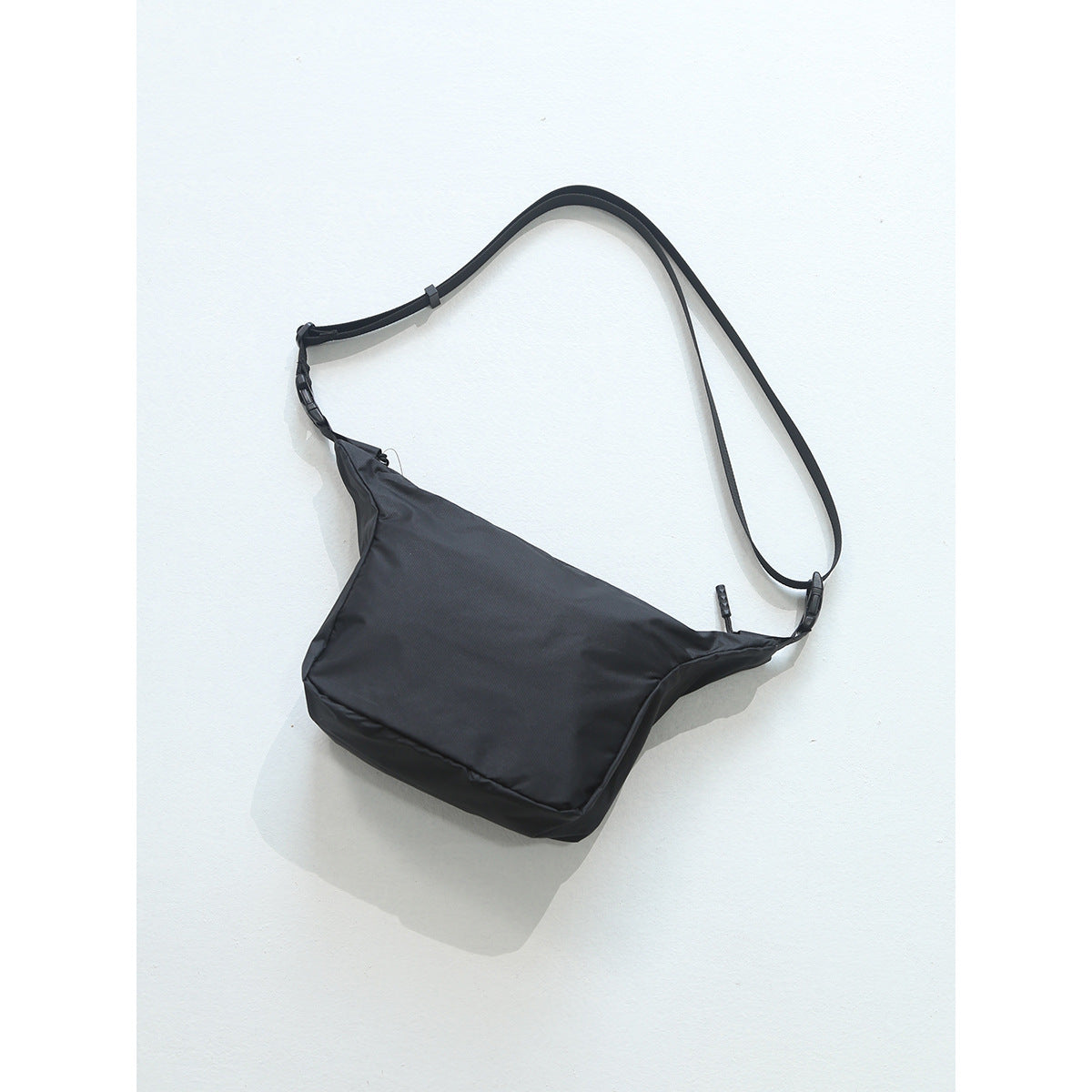 Black crossbody bag with adjustable black strap and side-release buckles on a light background