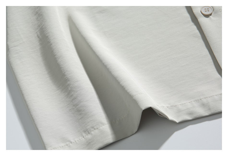 Close-up of the light ivory shirt's lower front, hem stitching, and a button.