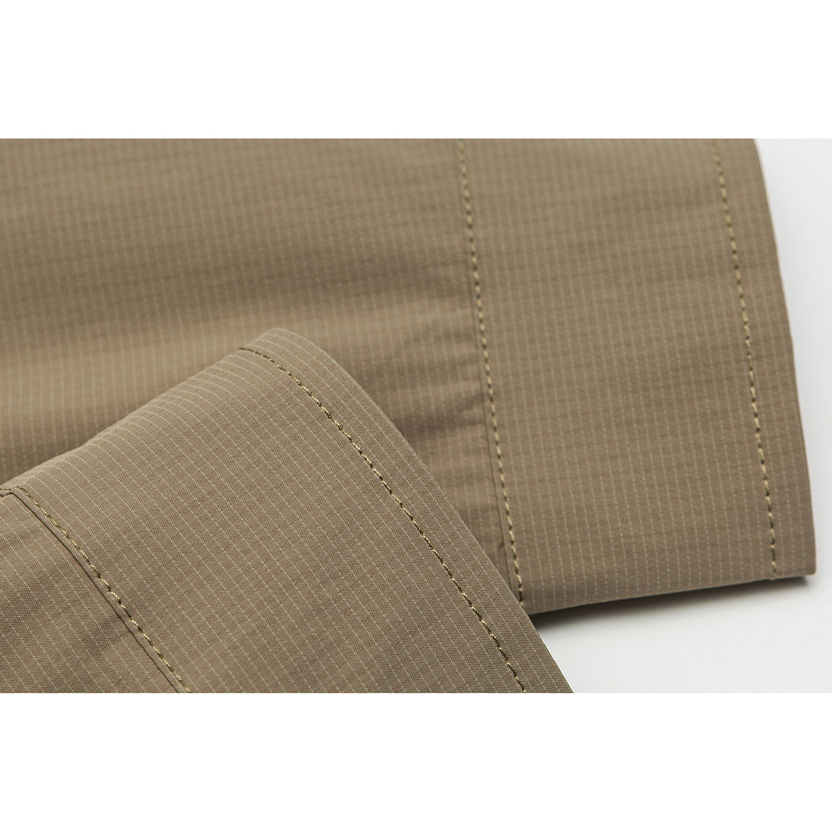 Close-up of taupe shirt fabric and stitching, showing a folded cuff and a straight seam.