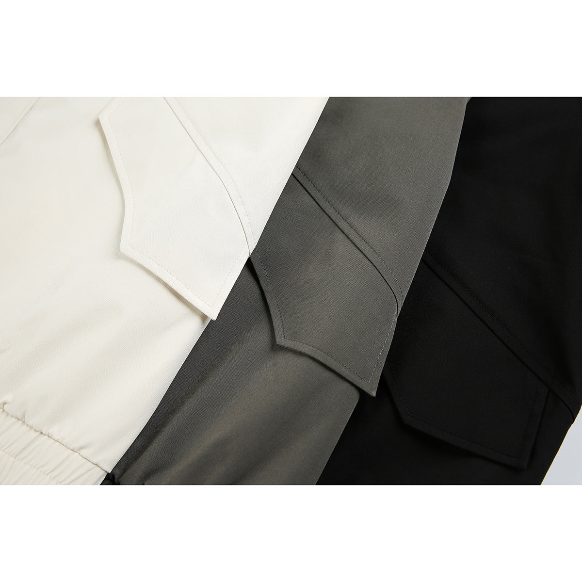 Close-up of cream, charcoal gray, and black jackets showing stitched sleeve or cuff panels.