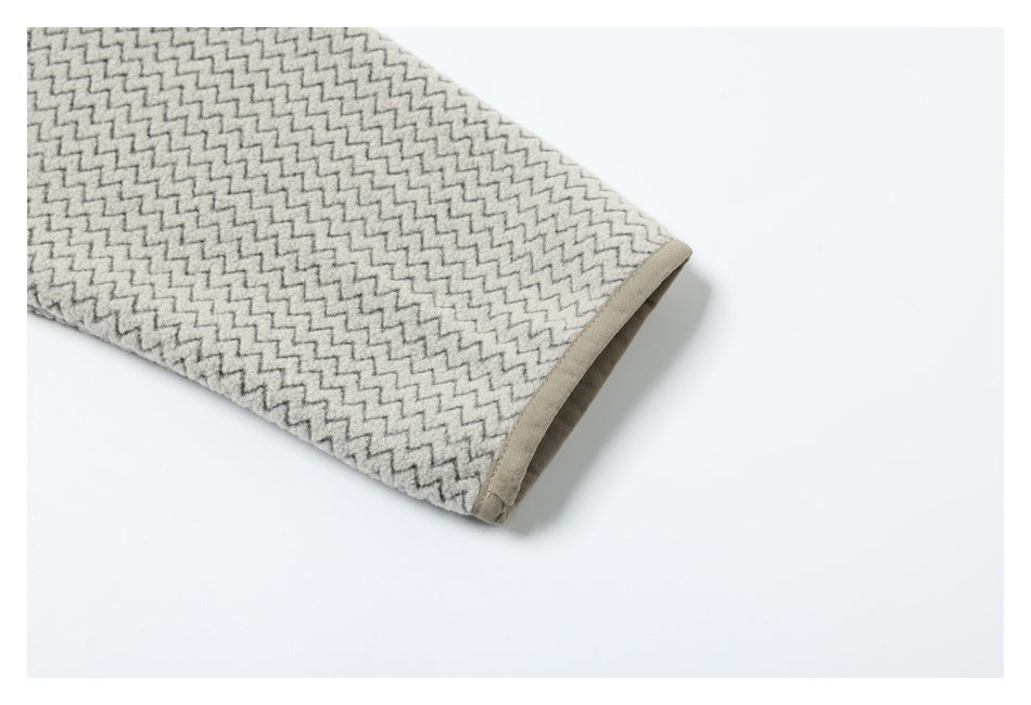 Close-up of a sleeve cuff with beige edge binding on cream and gray zigzag-patterned fabric.