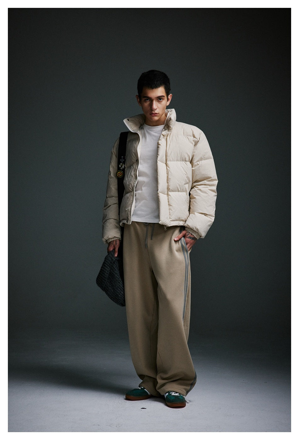 Model wearing an ivory puffer jacket over a white shirt with loose taupe side-striped trousers.