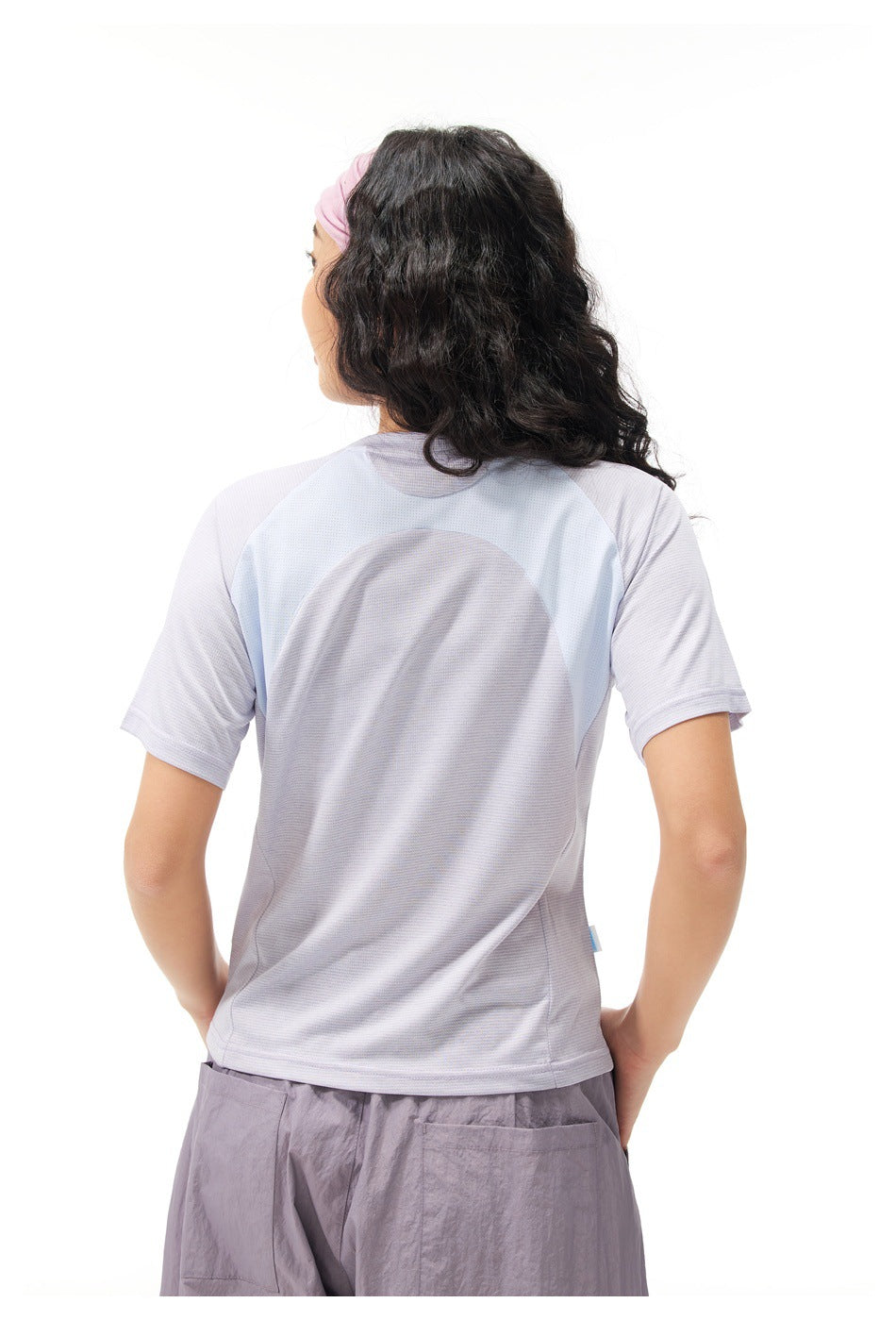 Rear view of a model wearing a pale lavender T-shirt with light blue shoulder panels and lavender-gray pants.