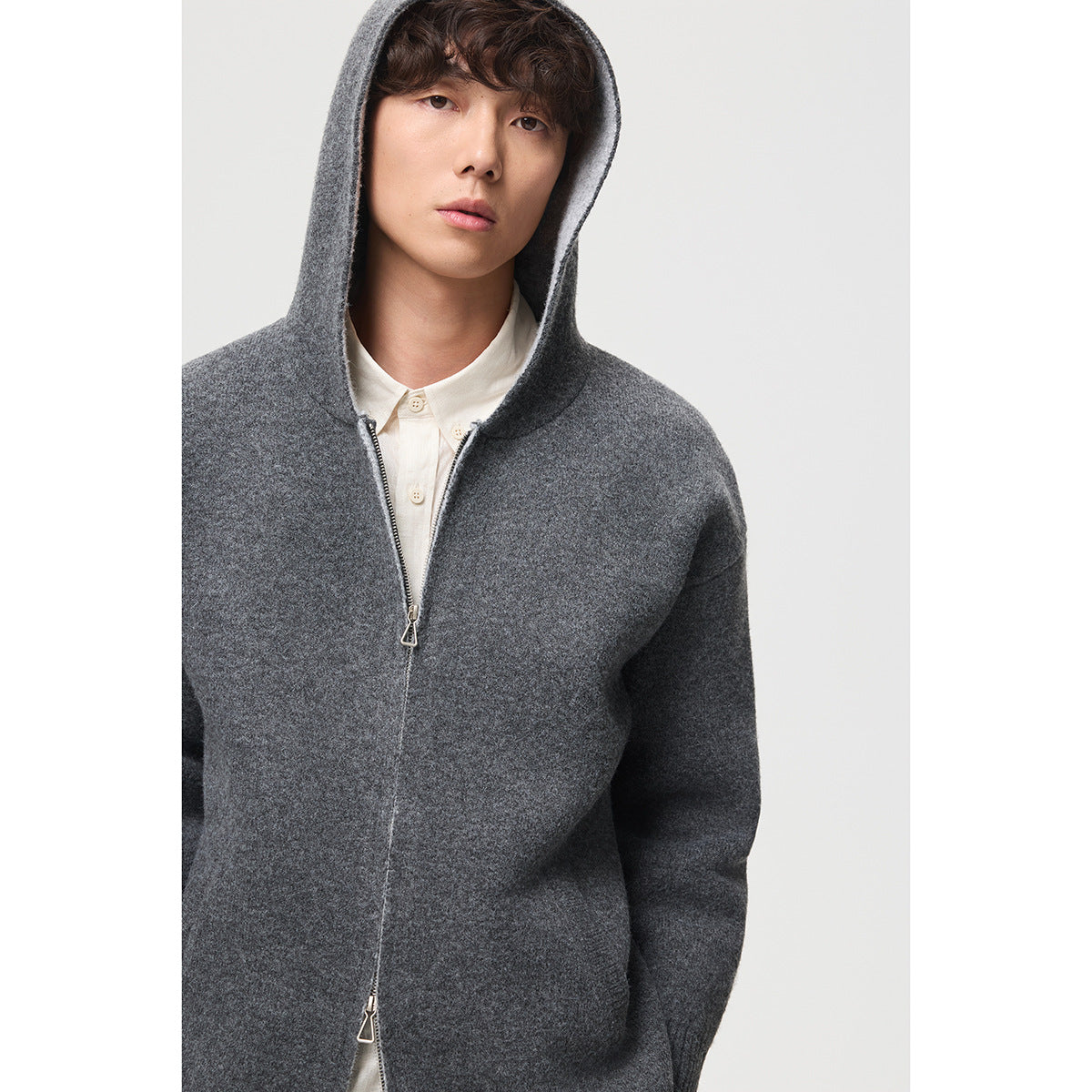 Model wearing a dark gray hooded knit jacket with a front zipper over a white shirt.