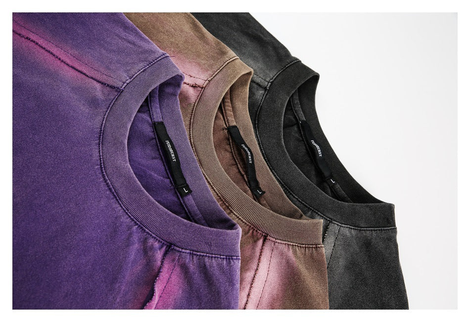 Close-up of purple, brown, and black crew-neck shirts arranged together, showing ribbed collars and inner labels.