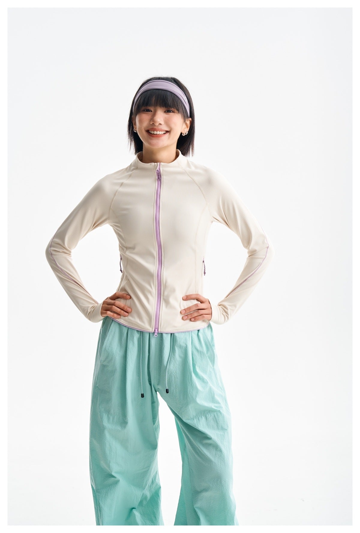 Front view of a model in an ivory zip-front jacket with lavender trim and mint-green trousers.
