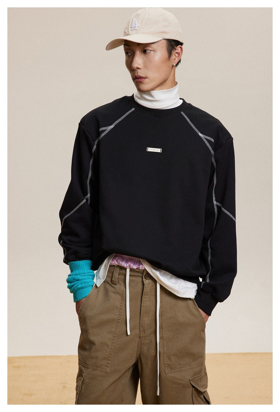 Close front view of a model wearing a black sweatshirt with contrast seams and a small chest label.