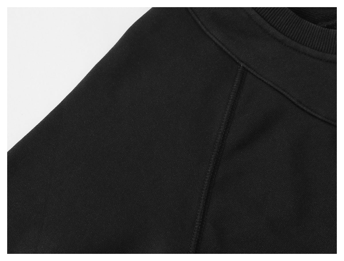 Close-up of a black garment's ribbed crew neck and shoulder seam against a white background.