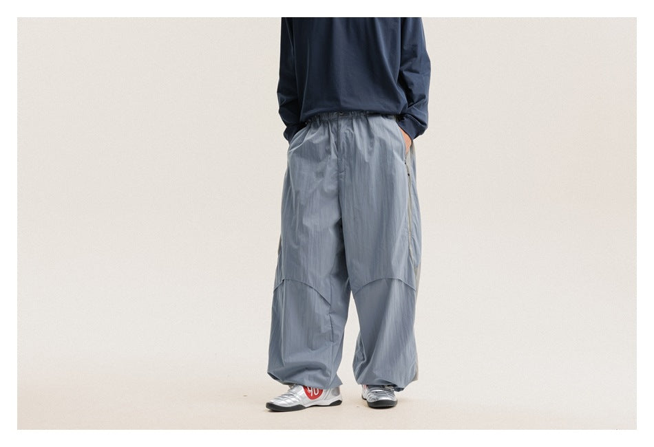 Model wearing loose slate-blue pants with an elastic waist, curved panel seams, and gathered cuffs, shown from the front.