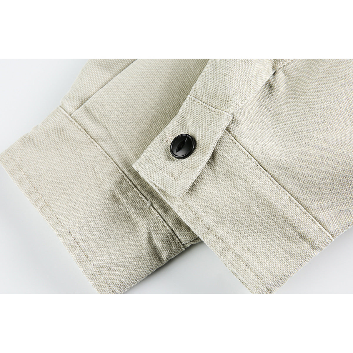 Close-up of a light beige jacket cuff with a black button and visible stitching.