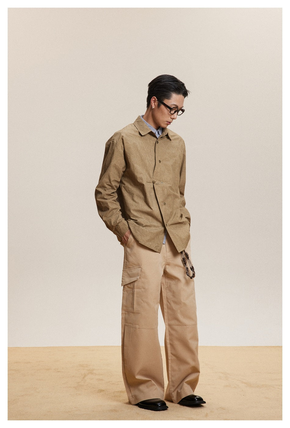 Model in a tan button-front shirt jacket with a waist tab and beige cargo pants, shown at a three-quarter angle.