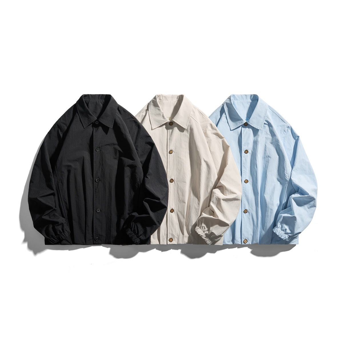 Three collared jackets with elastic cuffs shown from the front in black, off-white, and light blue.
