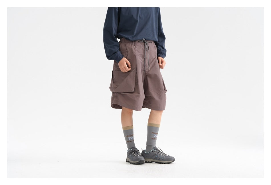 Cropped three-quarter view of a model wearing mauve-gray wide cargo shorts with a drawstring waist and large side pockets.