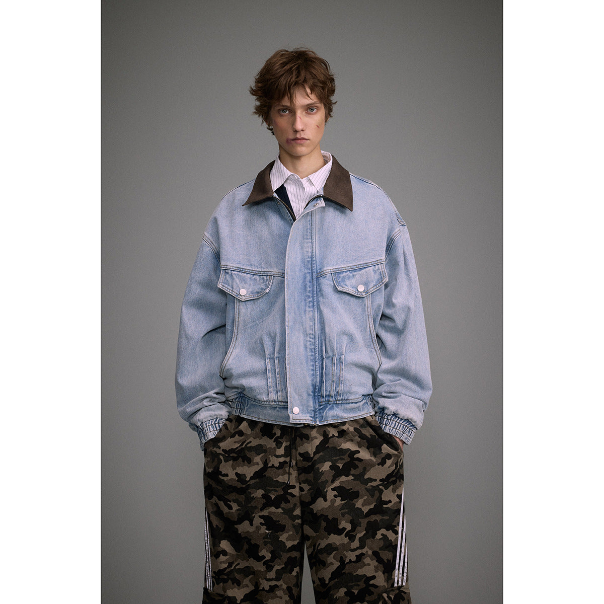 Front view of a model in a light blue denim jacket with a brown collar, paired with camouflage trousers.