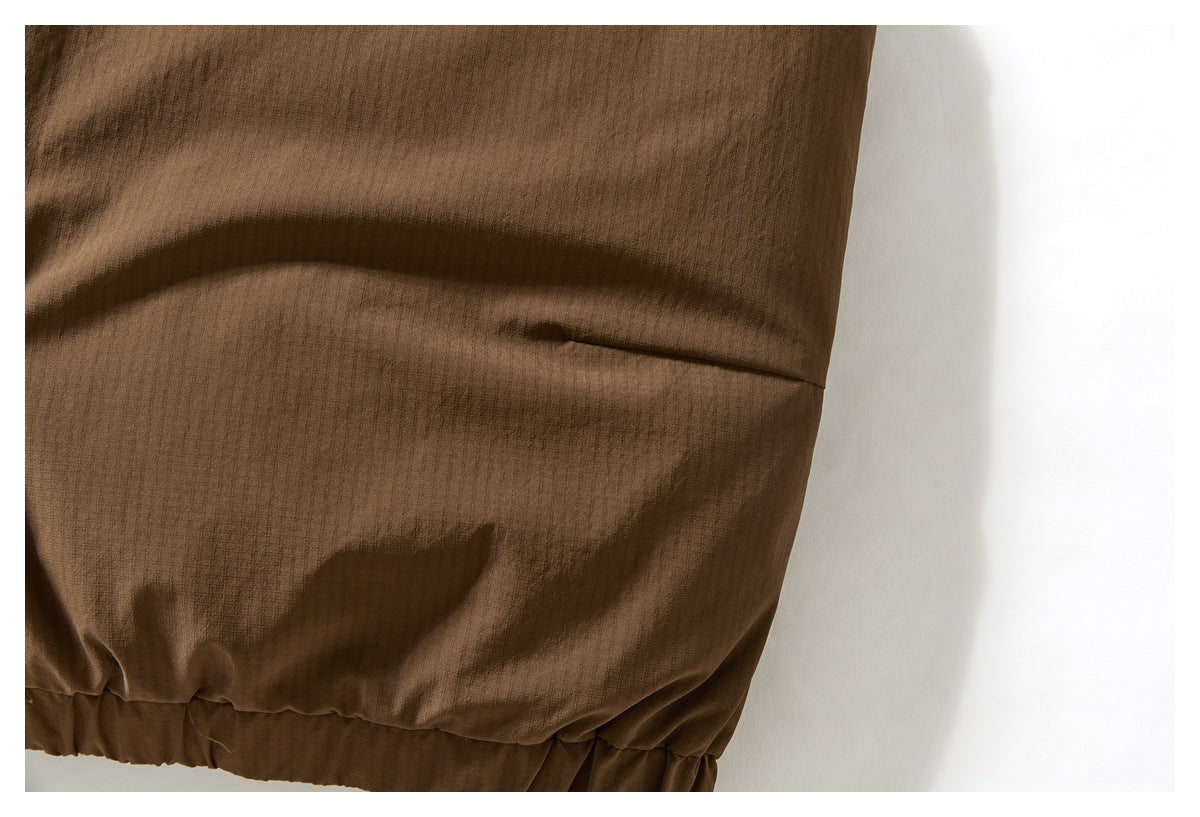 Close-up of a brown jacket hem showing a seam, gathered elastic edging, and textured fabric.