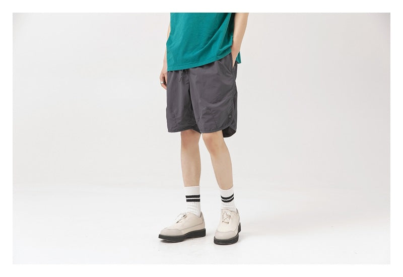 Cropped model view of charcoal gray shorts with side pocket, worn with a teal shirt and white shoes.