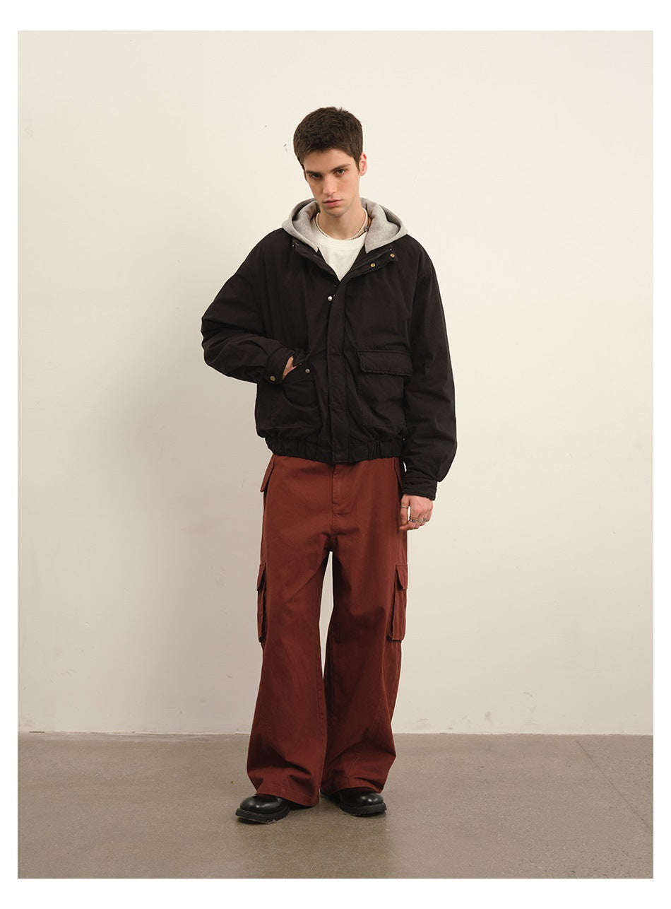 Model wearing rust-red wide-leg cargo trousers and a black jacket over a gray hooded top.