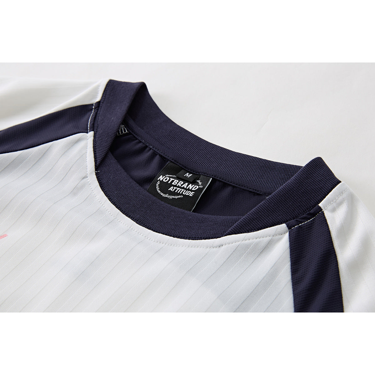 Close-up of a white jersey with a navy ribbed crew neck and shoulder panels; the sewn neck label is visible.