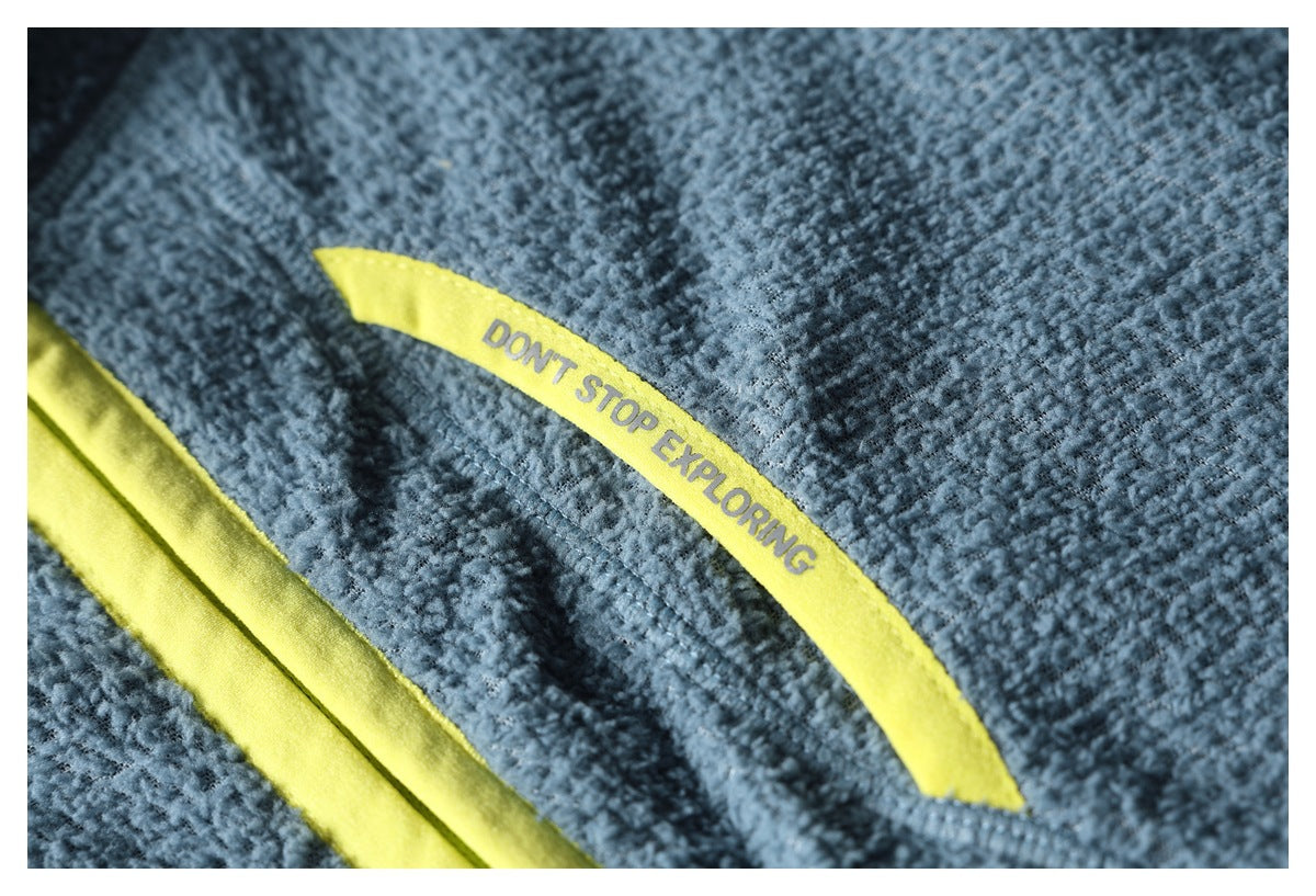 Close-up of a blue textured fleece jacket pocket with yellow-green trim and the words “DON'T STOP EXPLORING.”