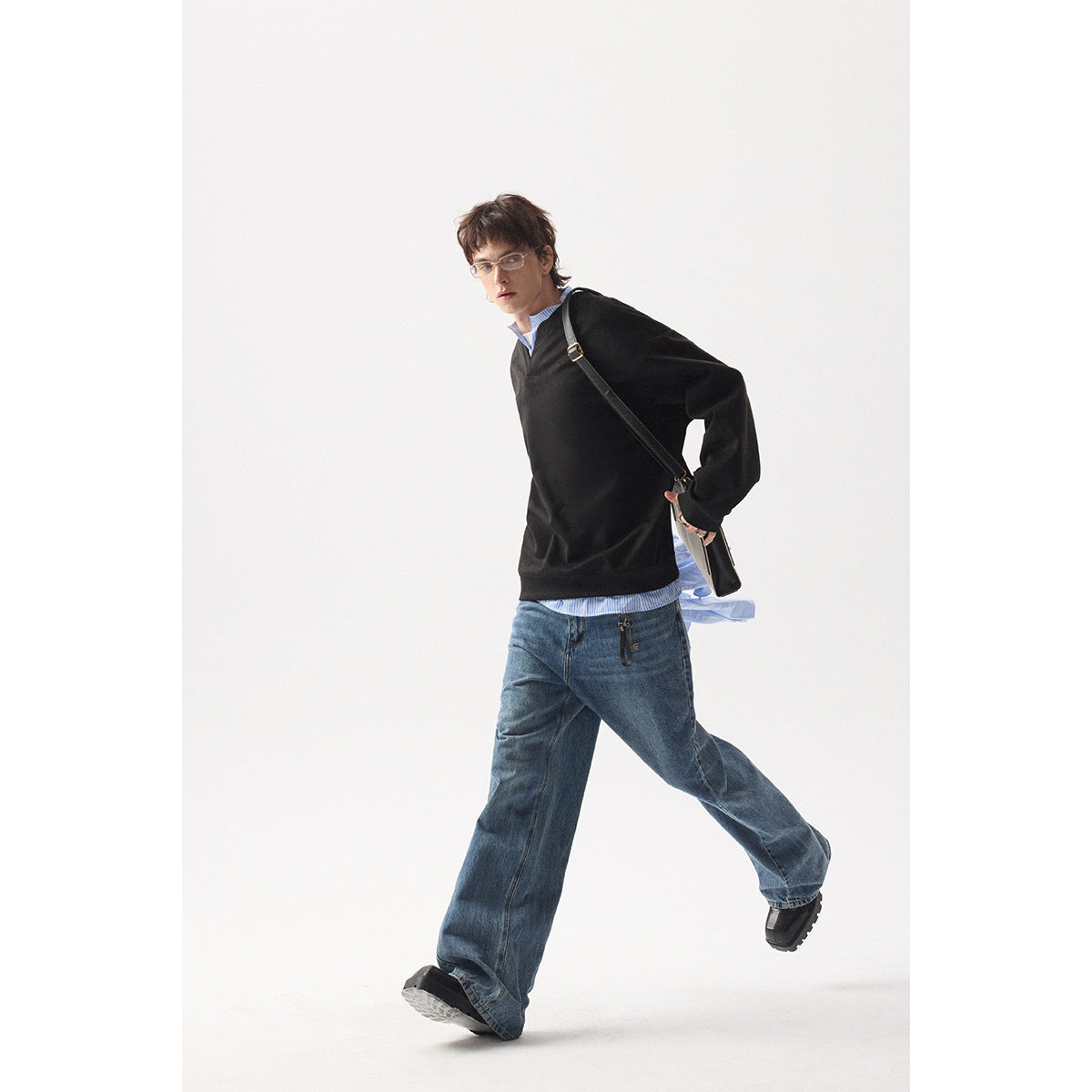 Model wearing a black V-neck sweatshirt over a blue striped shirt with loose blue jeans.