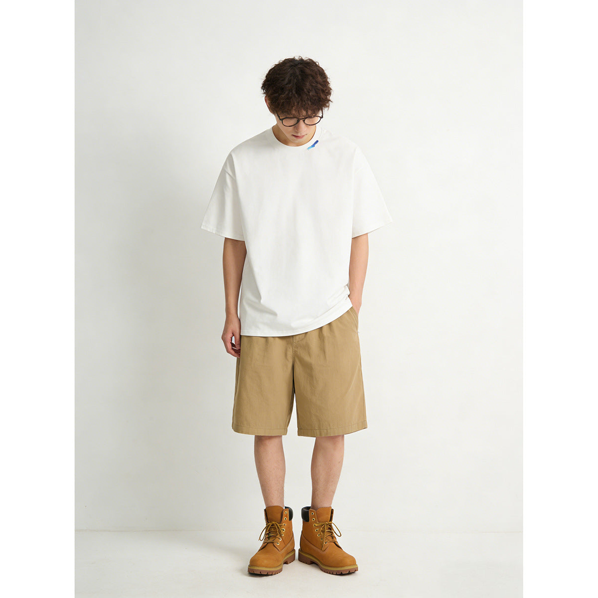 Model wearing an oversized white short-sleeve T-shirt with a small blue neckline detail and tan shorts.