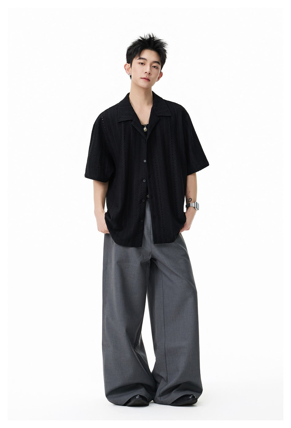 Full-length front view of a model in a black openwork short-sleeve shirt and gray wide-leg trousers.