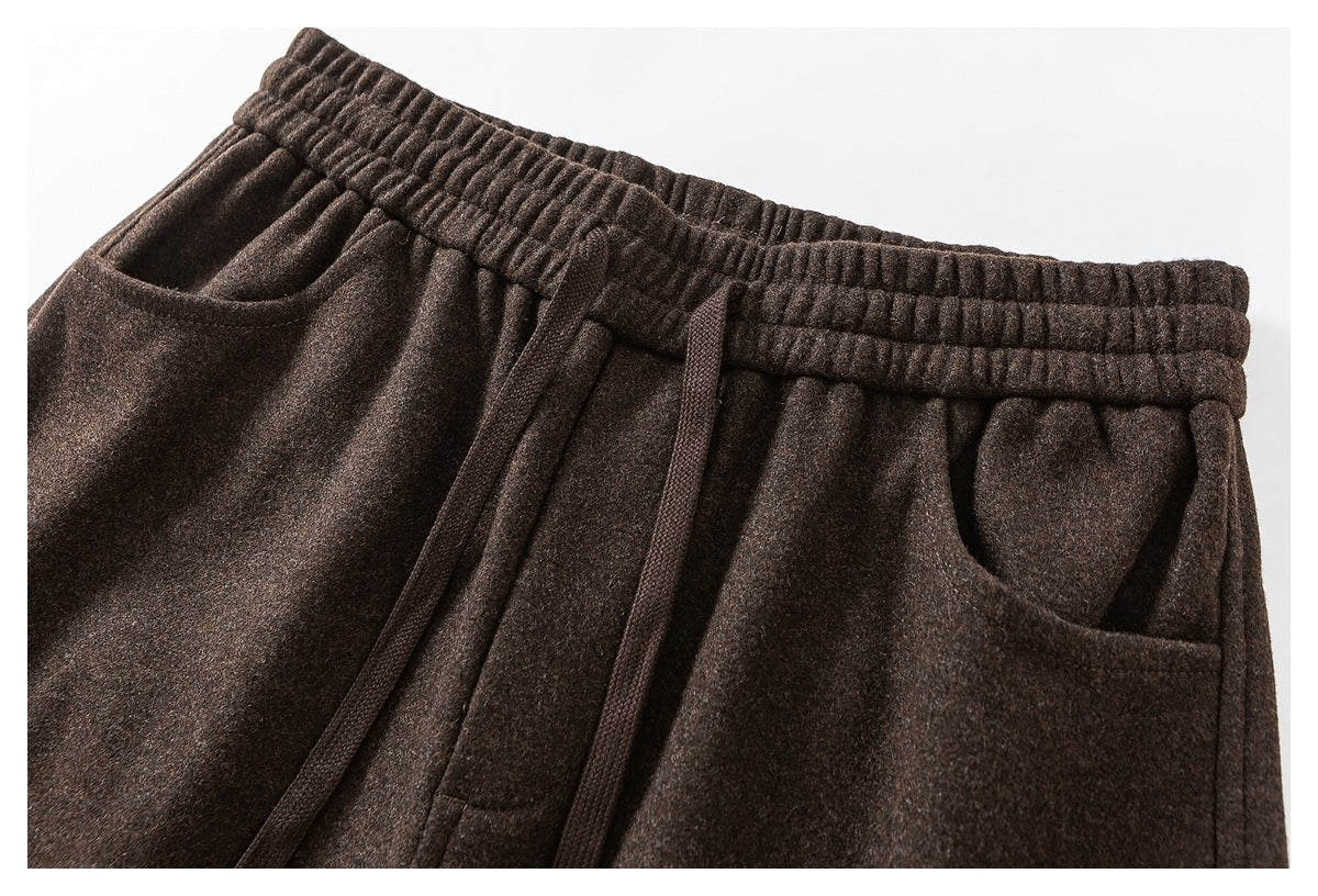 Close-up of dark brown pants showing an elastic waistband, drawcord, front pleats and slanted pockets.