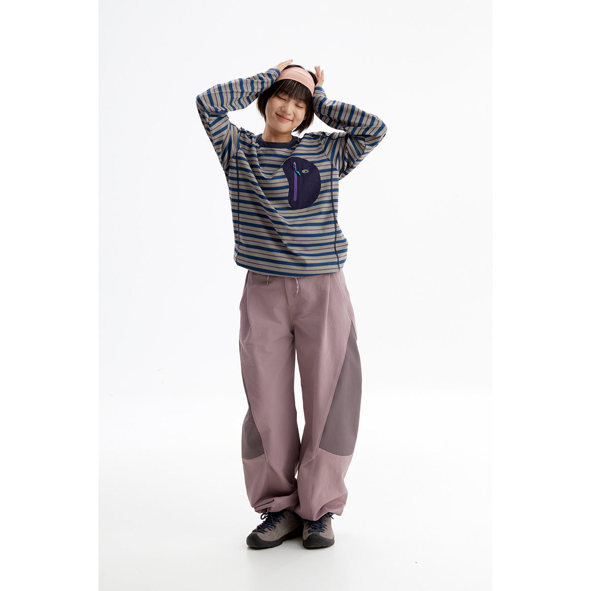 Model wearing a blue-gray striped long-sleeve top with a dark chest pocket and loose mauve pants.