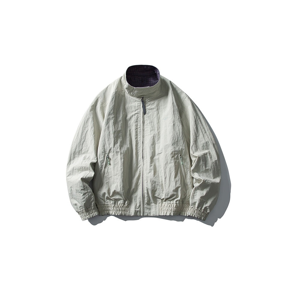 Pale gray zip-front jacket with a stand collar, two zip pockets, elastic cuffs and hem, and a small chest emblem.