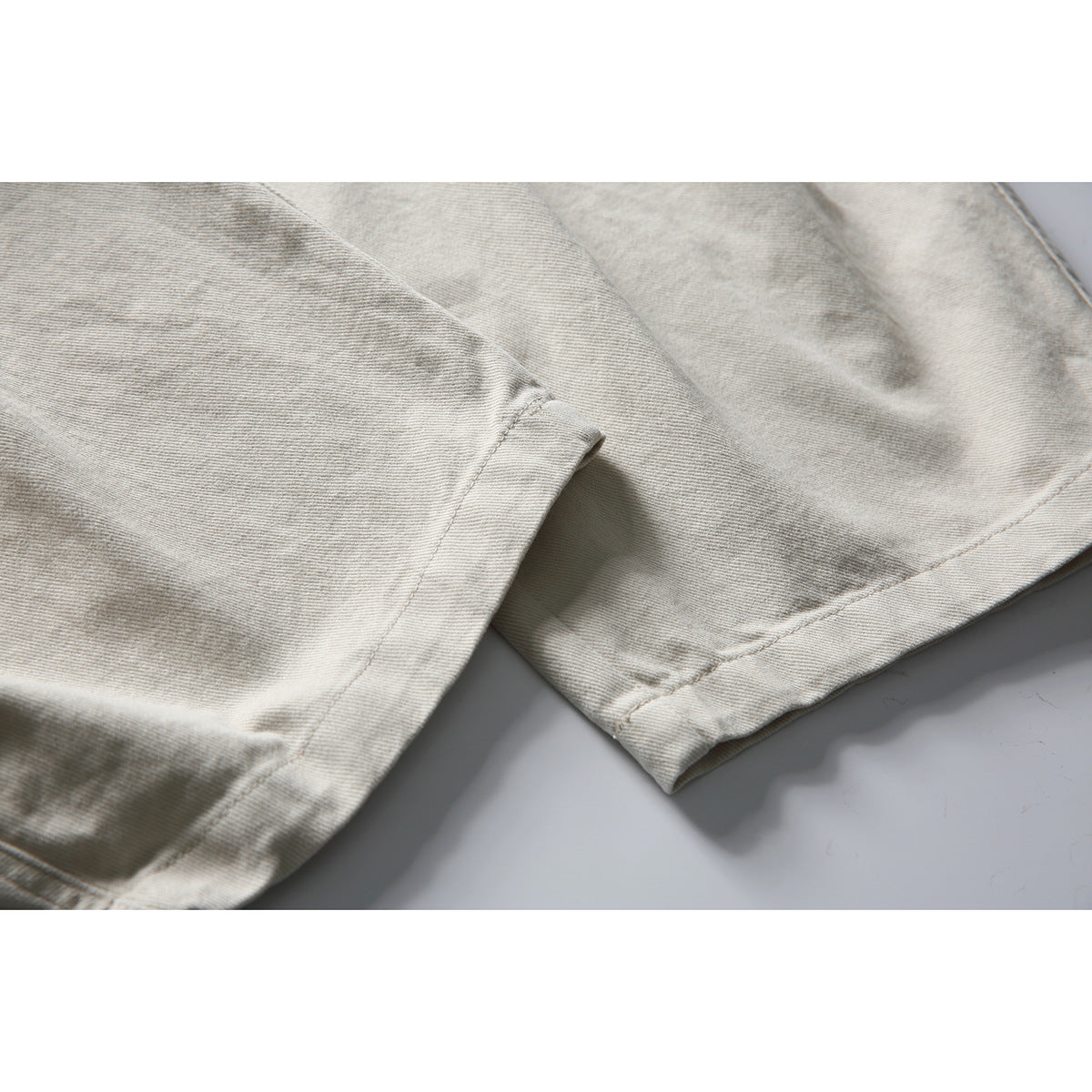 Close-up of the light beige trousers' wide legs and stitched hems.