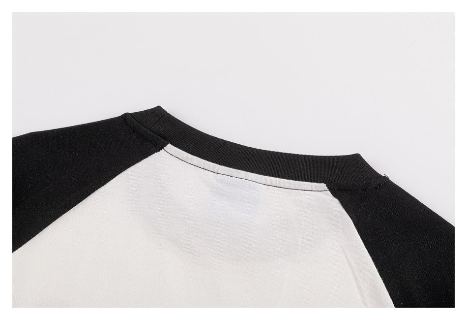 Close-up of the black ribbed crew neckline and raglan seams on an off-white shirt with black sleeves.