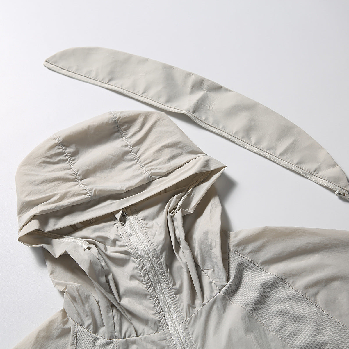 Close-up of a light beige hooded jacket with its hood spread open and a matching long zippered panel above it.