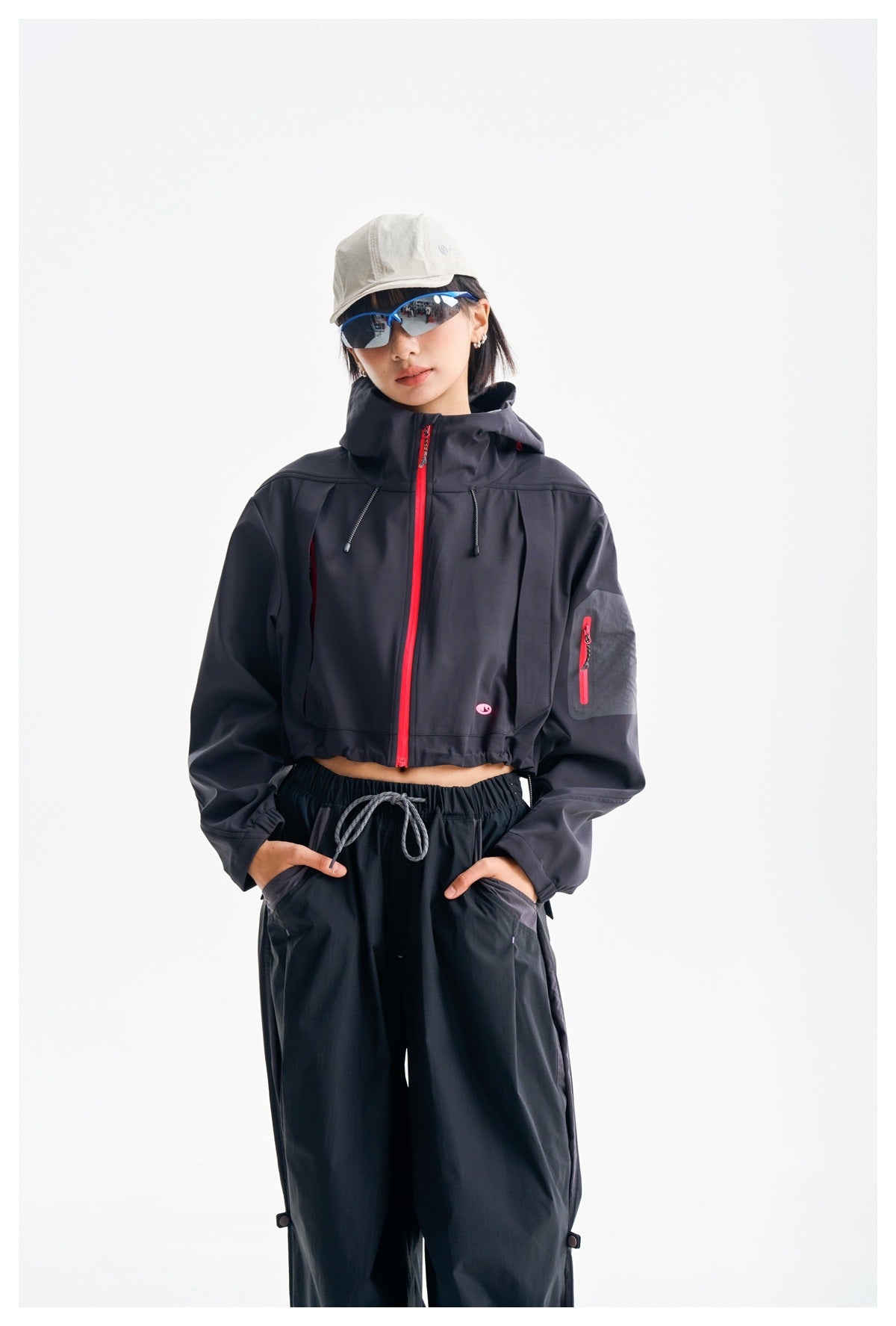 Closer view of a model wearing a dark hooded cropped jacket with a bright pink zipper and sleeve pocket.