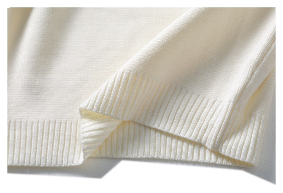 Close-up of an ivory knit sweater's ribbed hem and folded sleeve cuff.