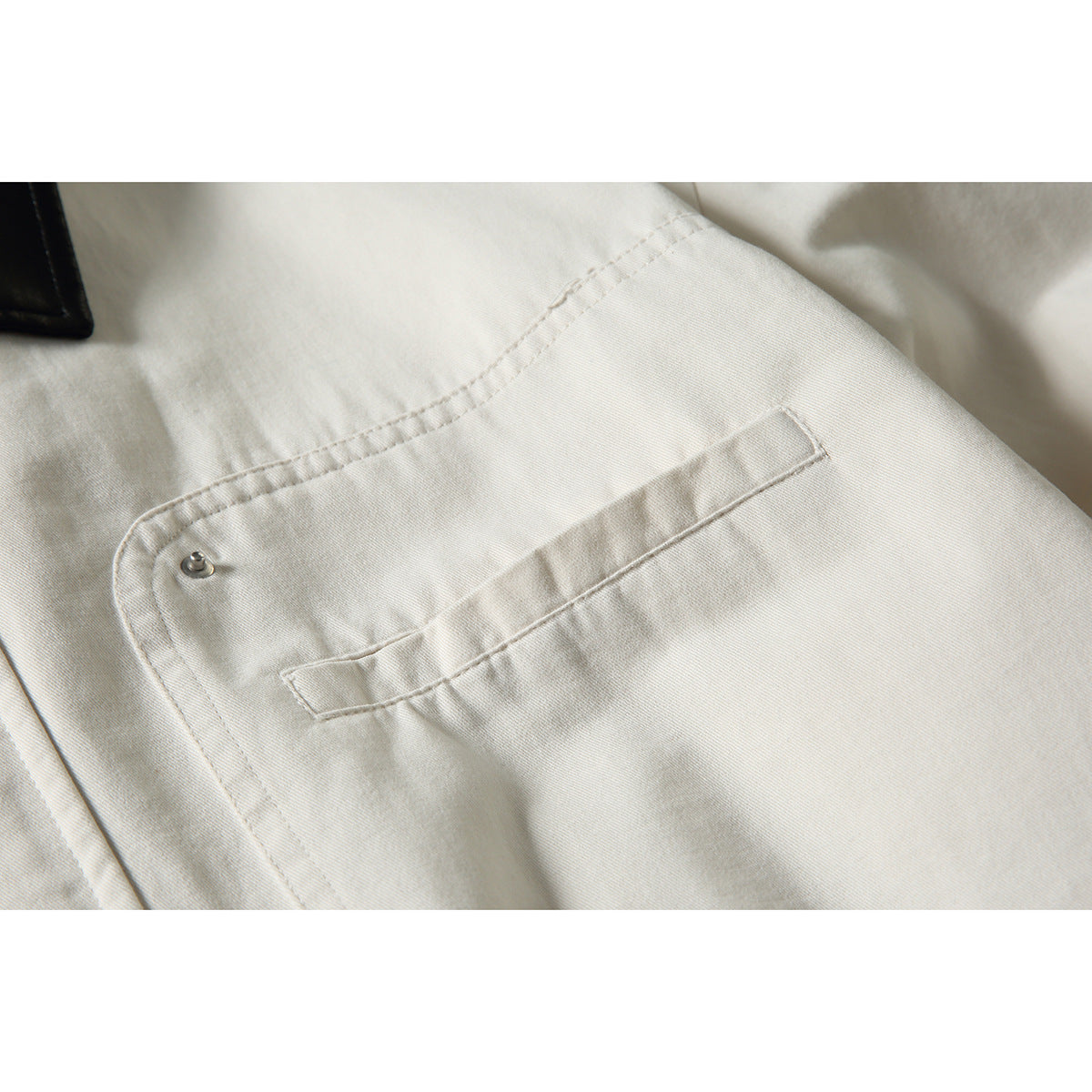 Close-up of an off-white jacket's stitched chest pocket with a small metal snap.