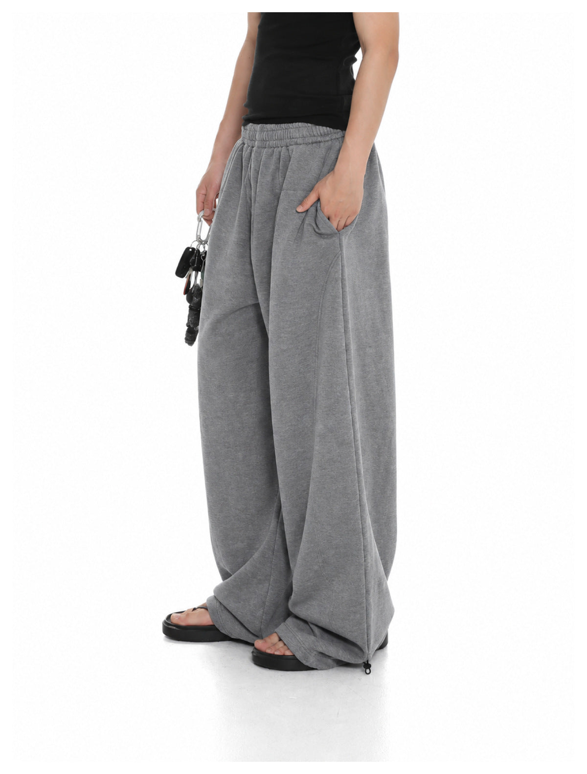 Person wearing gray wide-leg sweatpants with a black top and sandals, hand in the side pocket
