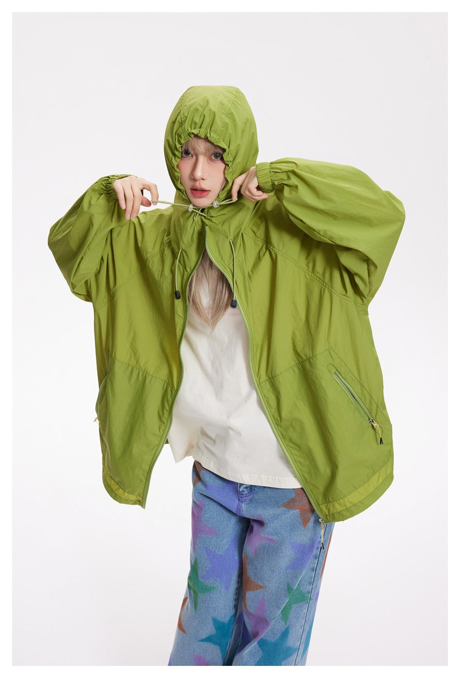 Model wearing a loose lime-green hooded jacket with front zipper and zip pockets, holding the hood drawcords.