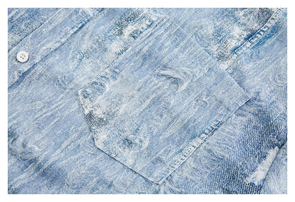 Close-up of a patch pocket on a light blue distressed denim shirt.