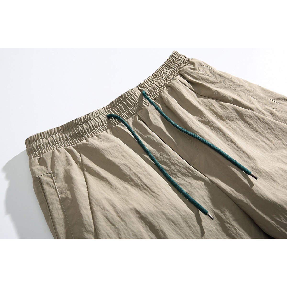 Close-up of beige pants with an elastic waist, teal drawstrings, and a side pocket.