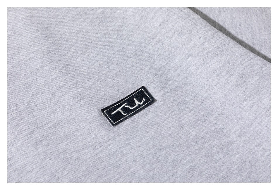 Close-up of a small black rectangular embroidered patch on light gray sweatshirt fabric.