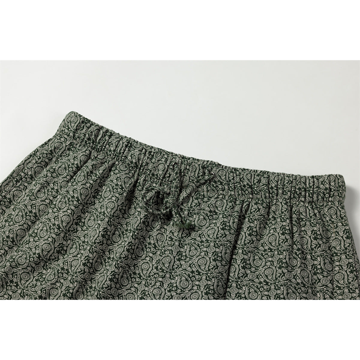 Close-up of dark green pants with a gathered waistband and drawstring, covered in a cream paisley print.