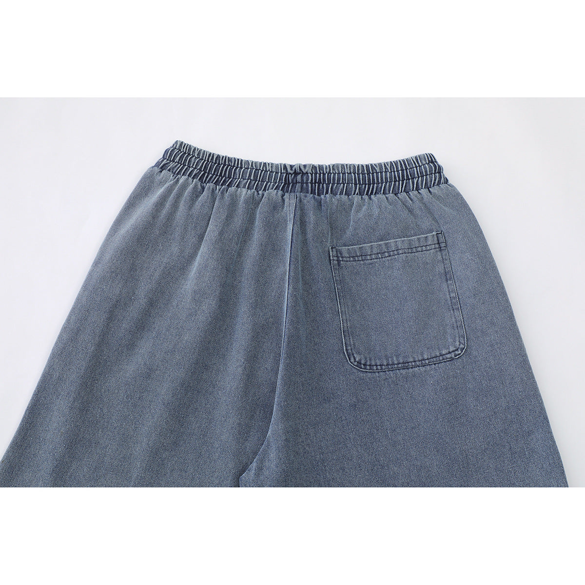 Back view of blue denim shorts with an elastic waistband and a single patch pocket.